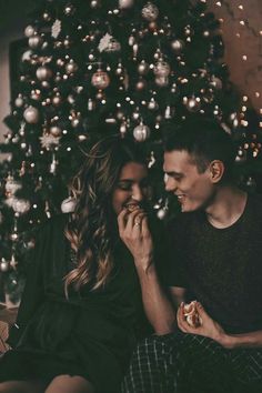 a man and woman sitting next to a christmas tree