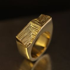 The Xyz Signature ring draws inspiration from modern architecture's Cartesian geometry and mineral structures. To balance against the minimalist solid, Agata hand-carved an intersting pattern on its front that imitates growing crystals forming parallel stritations on the surface. This intricate mineral pattern contrasts beautifully with high-polished surfaces of the ring. Made in 18k gold, this heavyweight ring stands out with its modernist and dynamic aesthetics. Despite its blocky and slightly brutalist appeal, the Xyz Signature ring seamlessly compliments the palm. Ideal future heirloom for mineral and architecture enthusiasts. Please note this ring is handmade and unique, so its texture may vary slightly from the one presented. Finer details: Material: 18k yellow gold. Measurements: 2. Growing Crystals, Signature Ring, Unique Mens Rings, Signature Rings, Mens Rings, Ring Stand, The Minimalist, Men's Rings, Modern Aesthetics