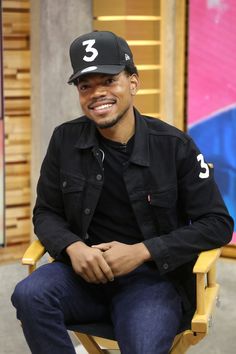 a man sitting in a yellow chair wearing a black hat and smiling at the camera