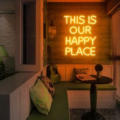 a neon sign that says this is our happy place next to a table with a guitar on it