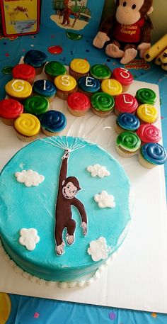 a birthday cake with a monkey on the top and cupcakes around it that spell out abc