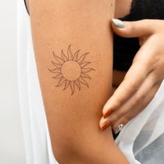 a woman's arm with a small sun tattoo on the back of her shoulder