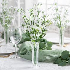 the table is set with white flowers and greenery in glass vases on it