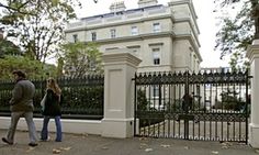 two people walking past a gate in front of a large white building with many windows