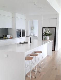 a white kitchen with three stools in front of the counter top and an island