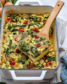 a casserole dish with spinach, tomatoes and cheese on top is being lifted by a wooden spoon