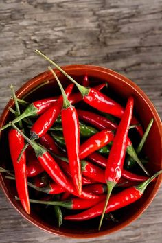 a bowl filled with red peppers on top of a wooden table