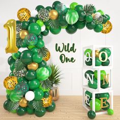 the balloon arch is decorated with green, gold and white balloons that read wild one