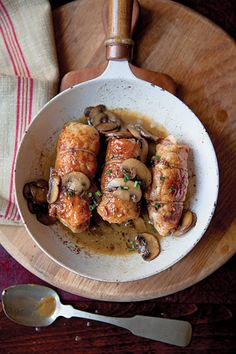 chicken with mushrooms and sauce in a white bowl on a wooden platter next to a spoon