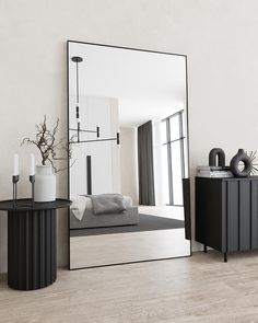 a large mirror sitting on top of a wooden floor next to a table and vase