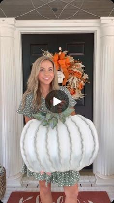 a woman standing in front of a door holding a large white pumpkin