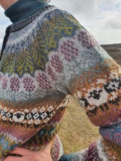 a woman standing in the middle of a field with her hands on her hips wearing a colorful sweater