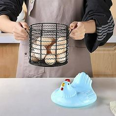 a person holding an egg in a wire basket next to a plastic toy chicken on a counter