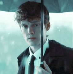 a young man holding an umbrella in the rain while wearing a suit and tie,