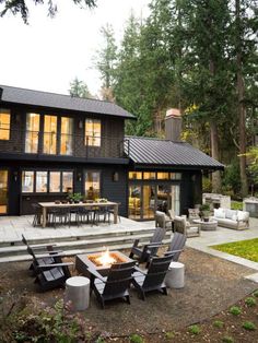 a fire pit sitting in front of a black house with lots of chairs around it