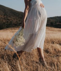 a woman in a white dress walking through tall grass