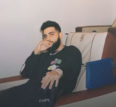 a man with a beard sitting on a couch next to a blue purse and looking at the camera