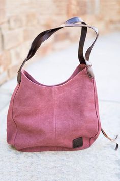 a pink purse sitting on the ground next to a brick wall with a brown strap