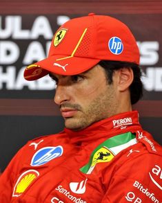 a man wearing a red hat and sitting in front of a wall with ferrari logos on it