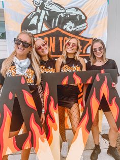 three girls are posing in front of an orange and black sign with flames on it