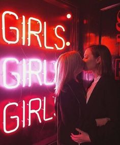 two women standing next to each other in front of a neon sign that says girls, girl