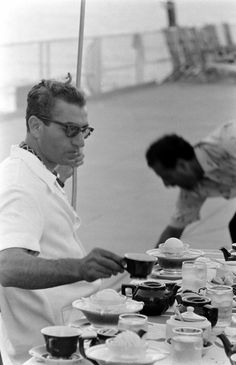 black and white photograph of two men eating at an outdoor table with tea cups on it