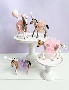 three miniature horses are standing on top of a cake plate with balloons in the air