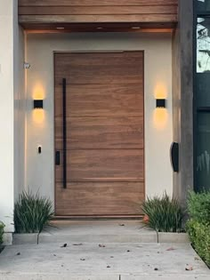 the front door to a modern home with lights on and plants in pots next to it