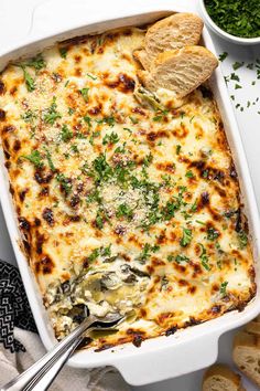 a casserole dish with cheese and spinach on the side next to bread