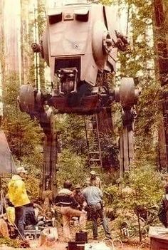 a group of people standing around a giant robot in the middle of a tree filled forest