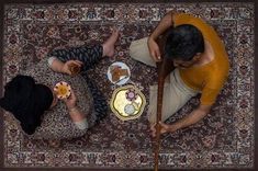 two people sitting at a table with food on top of it and one person holding a stick