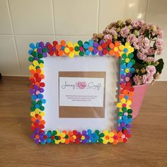 there is a colorful frame with flowers in it on the table next to a potted plant