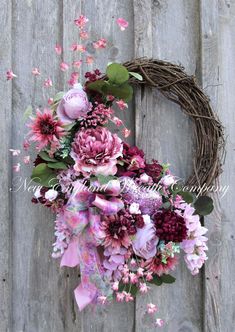 a wreath with pink flowers and greenery hanging on a wooden wall next to a fence