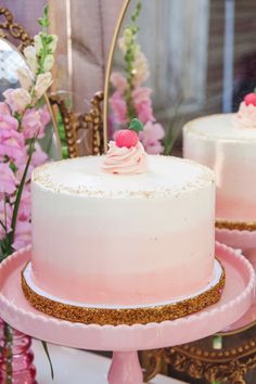 two pink cakes with white frosting and gold trim sitting on top of a table