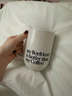 a woman is holding a coffee mug in her hand on a bed with white sheets