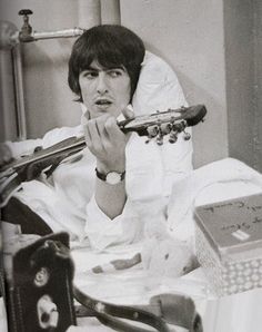 a man laying in bed holding a guitar