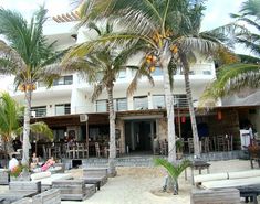 people are sitting at tables under palm trees on the beach in front of a hotel