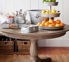 an assortment of fruit is displayed on a round table with baskets and utensils