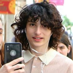 a woman with curly hair is looking at her cell phone while standing in the street