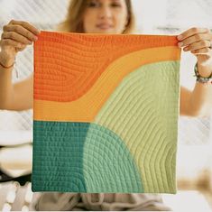 a woman holding up an orange and green piece of art that is in front of her face