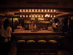 a bar with stools in front of it and people standing at the bar looking on