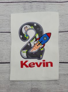 a white shirt with the number two on it and a rocket ship in the center