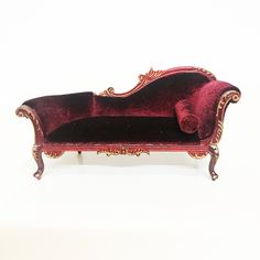 a red velvet couch with gold trimmings on the back and arms, sitting against a white background