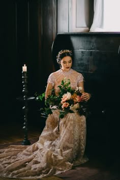 a woman in a wedding dress sitting on a chair with flowers and candles around her