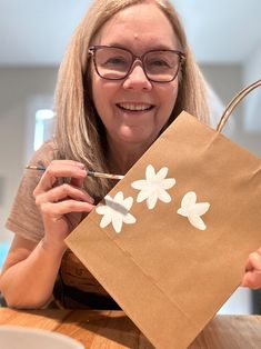 a woman holding a brown paper bag with white flowers on it, while sitting at a table