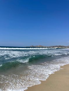 the ocean waves are rolling in and out of the water on a sunny day with clear blue skies