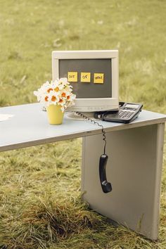 an old computer sitting on top of a desk with a phone and flower pot next to it