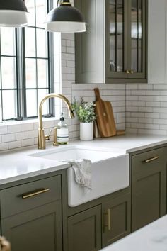 a kitchen with green cabinets and white subway backsplash, brass faucet