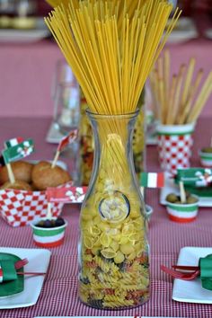 a vase filled with pasta sitting on top of a table next to plates and cups