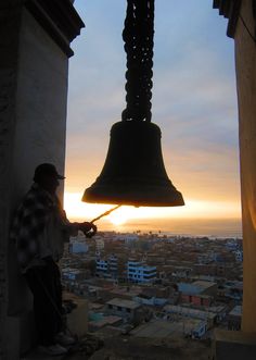 a bell hanging from the side of a building next to a person standing in front of it